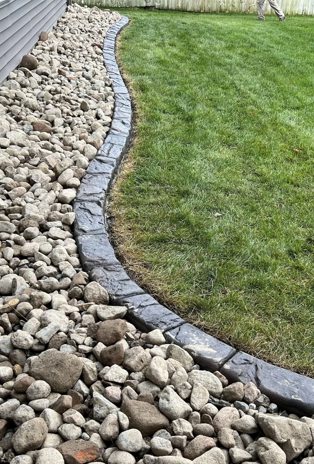 Curved stone pathway alongside rocks and grass in a landscaped yard.