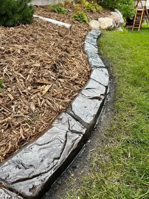 Curved stone edging along a mulched garden bed with green grass and landscaping.