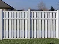 White vinyl fence with vertical slats, set against a blue sky and green lawn.