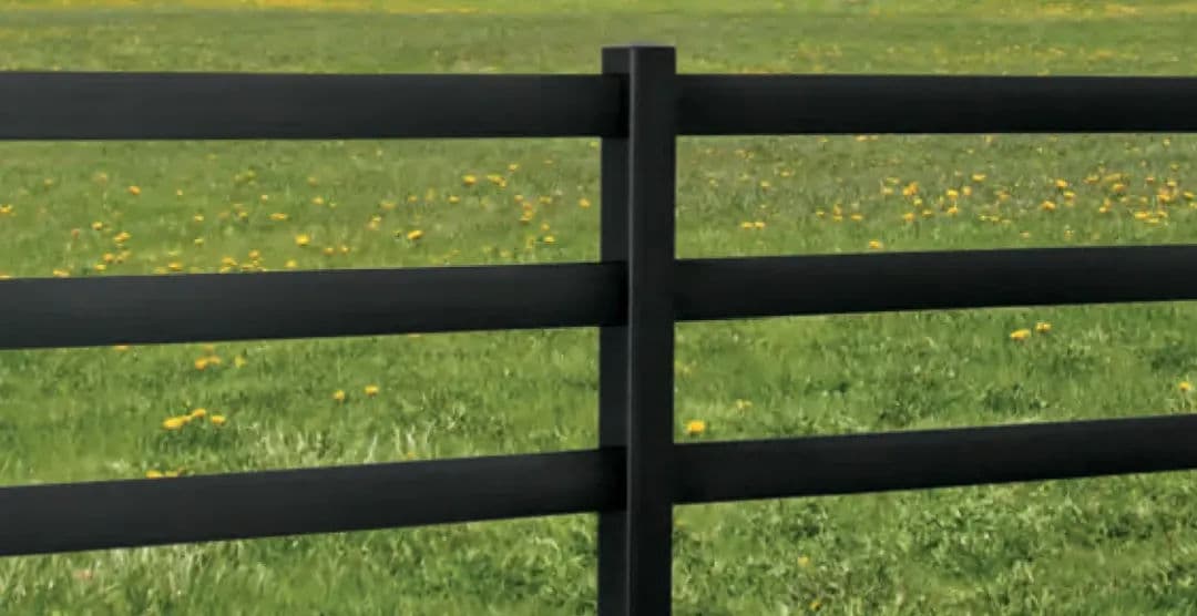 Black wooden fence against a green field with yellow dandelions.