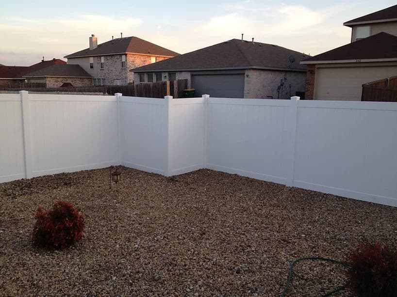 White privacy fence enclosing a gravel yard with shrubs under a clear sky.