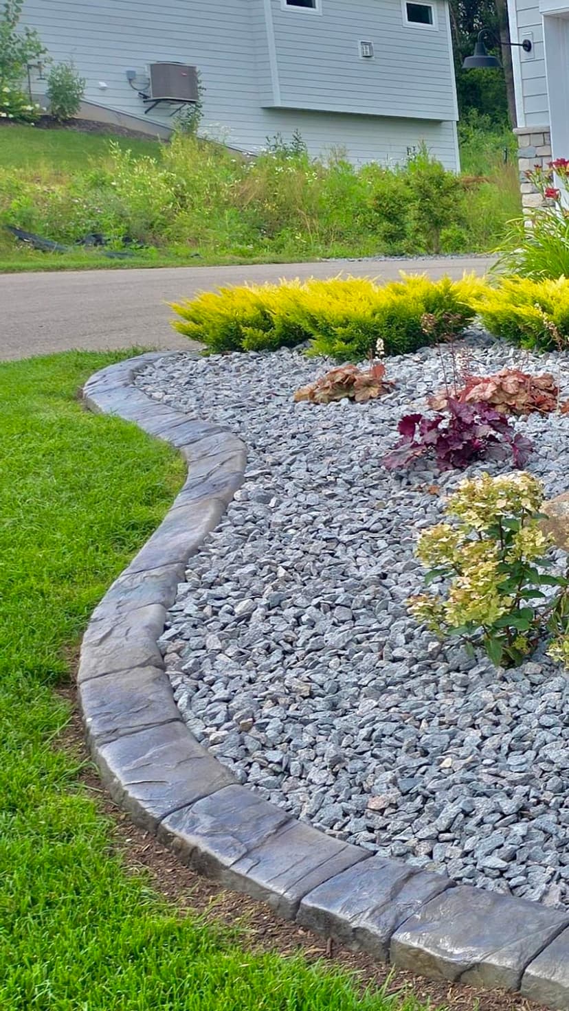 Lush garden with decorative stones, vibrant plants, and curved stone edging along a driveway.